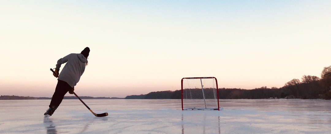 Ice Skater Enjoying A Winter Day At The Dymond Township Outdoor Rink In The City Of Temiskaming Shores Ontario Where The Rink Is Surrounded By Snow-Covered Trees With The Person Playing Ice Hockey Having Fun With Only A Hockey Stick Puck And Net